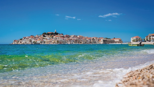 Una località costiera con edifici lungo la riva, acque blu cristalline e una barca sulla spiaggia.