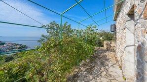 Un vialetto in pietra conduce a un edificio con vista su una cittadina costiera e sul mare.