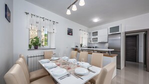 Zona de dinar moderna amb una taula llarga preparada per a quatre persones, parets blanques i una cuina al fons.