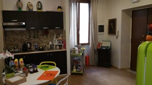 A compact kitchen with a dining table, a refrigerator, and a window with curtains. - A Casa Di Giò (Rome)
