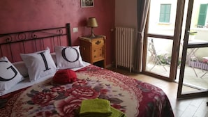 A bedroom with a bed, floral bedspread, pillows with letters, a nightstand, a lamp, a radiator, and a view of the outside. - A Casa Di Giò (Rome)
