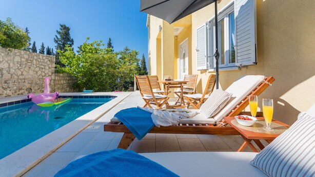 A poolside area with lounge chairs, a table with drinks, and a stone wall. - Villa Zlata (Zupa dubrovacka)