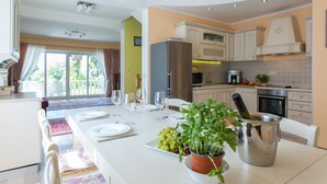 A modern kitchen with white cabinets, a stainless steel refrigerator, and a dining area with a table set for four. - Villa Zlata (Zupa dubrovacka)