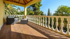 A covered outdoor area with a wooden ceiling, a white balustrade, and a seating area with a sofa and table. - Villa Zlata (Zupa dubrovacka)