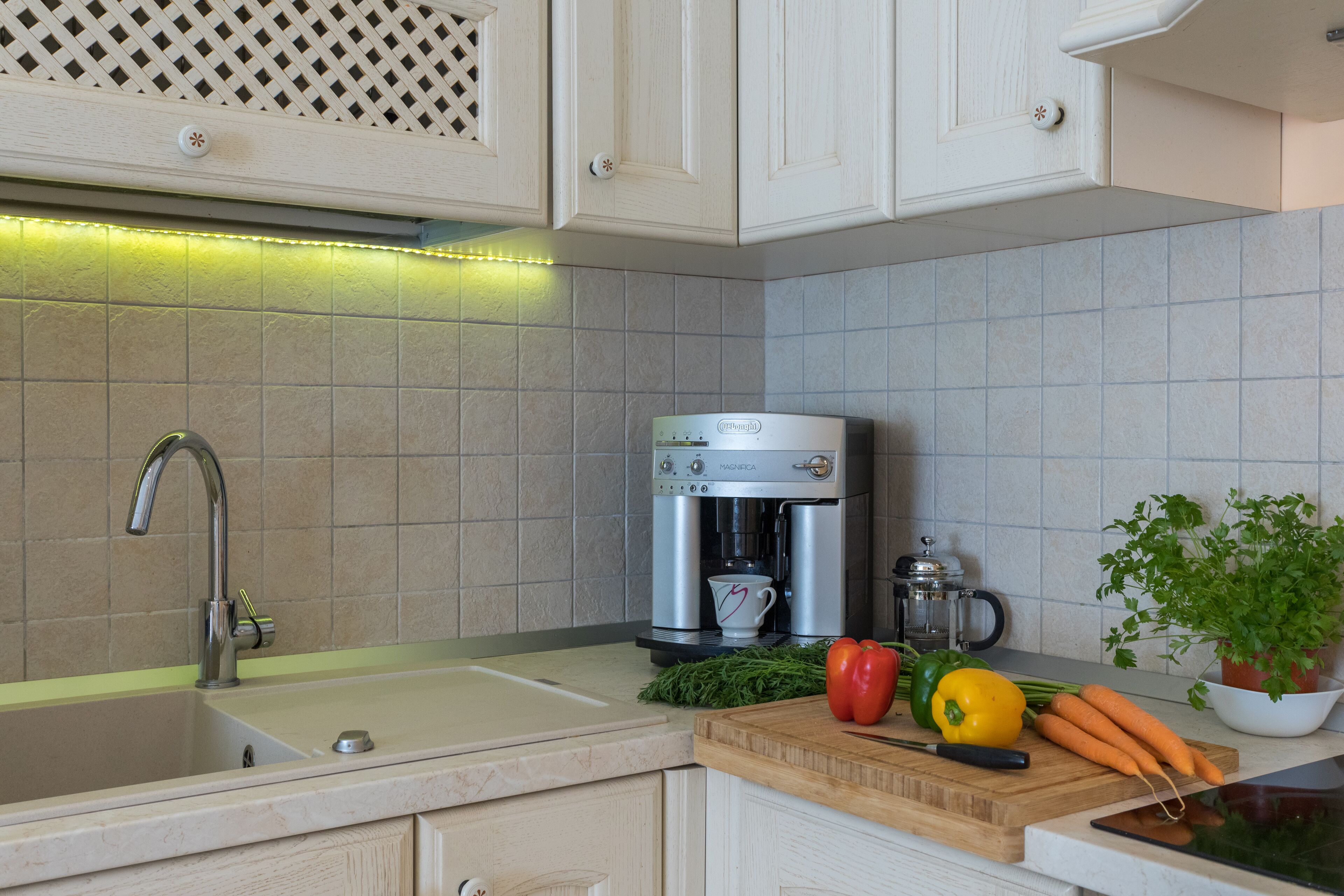 Une cuisine équipée d’un évier, d’une machine à café, d’une planche à découper avec des légumes et d’une plante en pot.