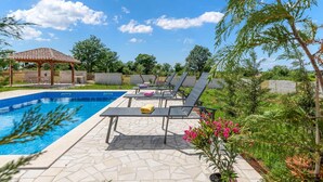 A swimming pool with lounge chairs, a pergola, and a garden area.