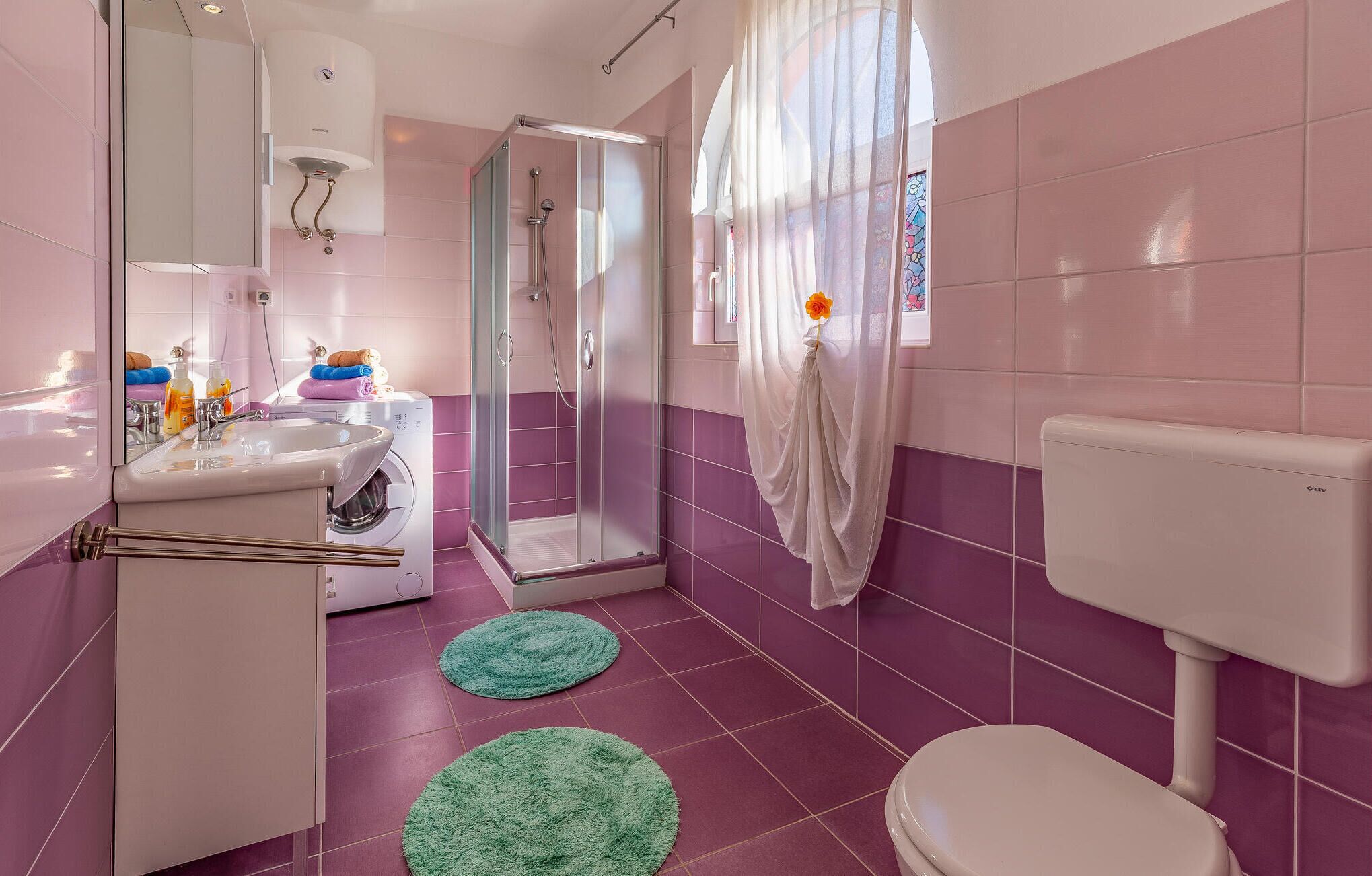 Un bagno con piastrelle rosa, box doccia in vetro, un water bianco e un lavandino con specchio.