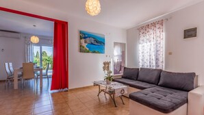 A modern living room with a sofa, a dining table with chairs, a red curtain, and a painting of a landscape.