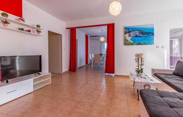 A modern living room with a flat-screen TV, a sofa, a dining area with chairs, and a red-framed doorway leading to another room. - Amazing home in Sisan (Sisan)