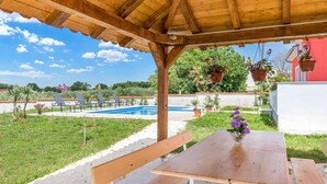A wooden pergola with a pool, lounge chairs, and a table with a vase of flowers.