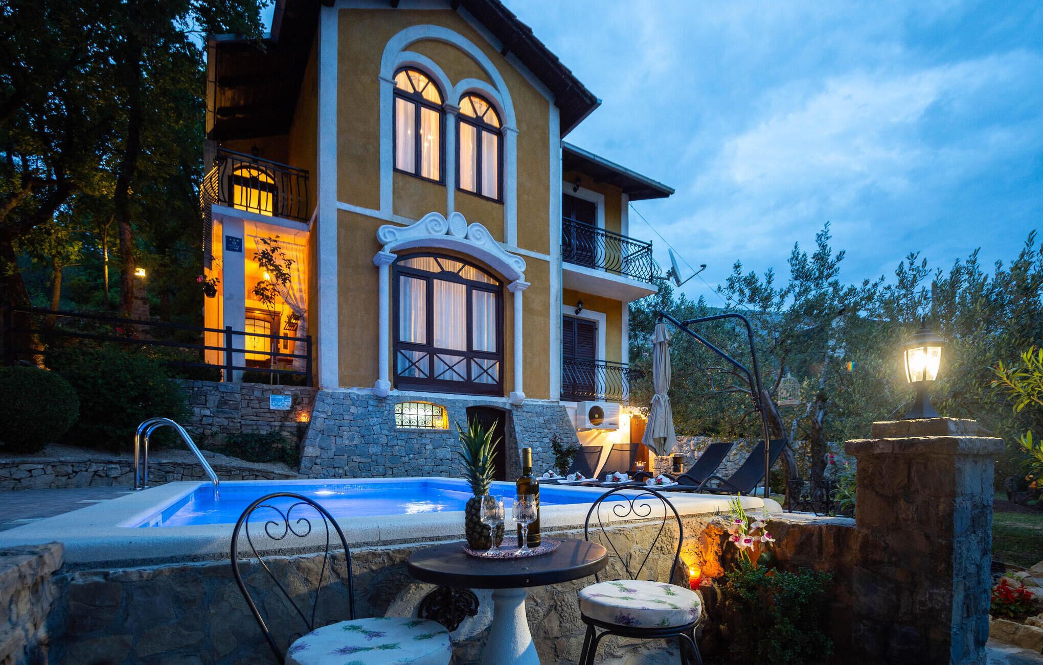 Eine luxuriöse Villa mit Swimmingpool, Sitzgelegenheiten im Freien und einem gut beleuchteten Eingangsbereich.