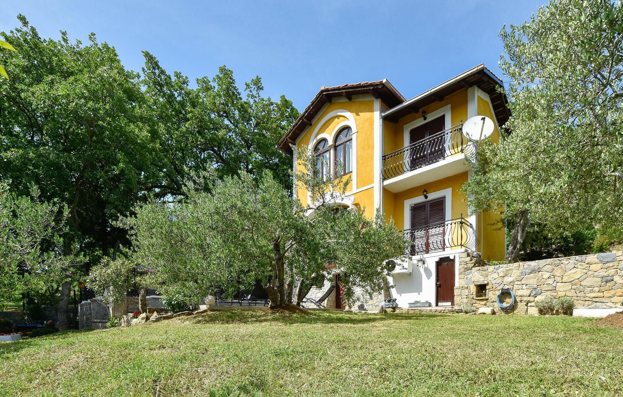 A two-story yellow building with a stone wall, a balcony, and a satellite dish.