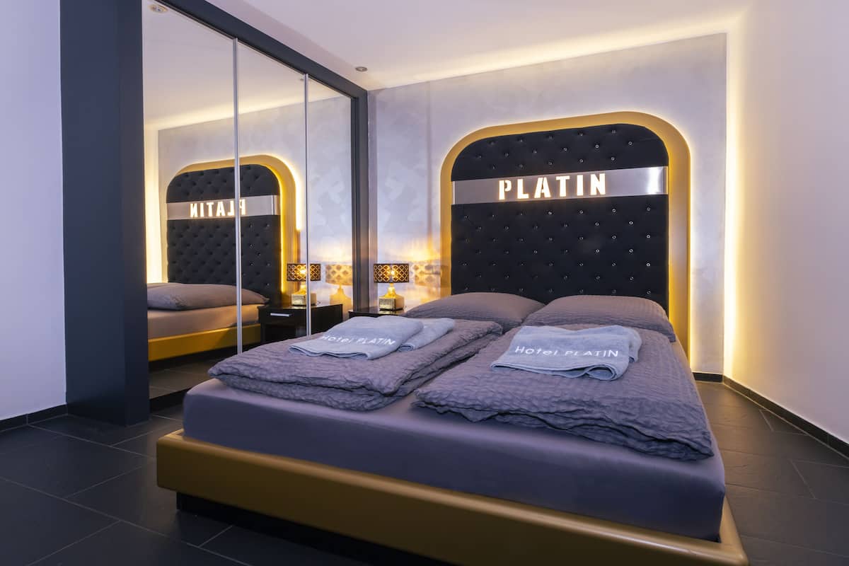 Een moderne hotelkamer met een groot bed, een spiegelwand en een hoofdeinde met de naam 'PLATIN'.