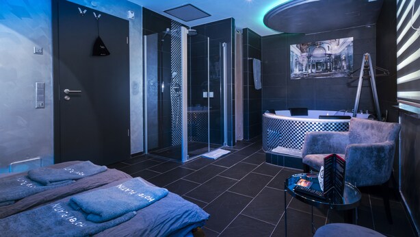 Une salle de bain moderne avec une douche en verre, une baignoire, un meuble-lavabo avec un miroir et un coin salon comprenant une chaise et une petite table.