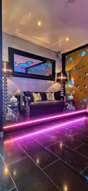 A modern living room with a dark-colored sofa, a large mirror, and a wall with circular cutouts. - Hotel Platin Regensburg (Regensburg)