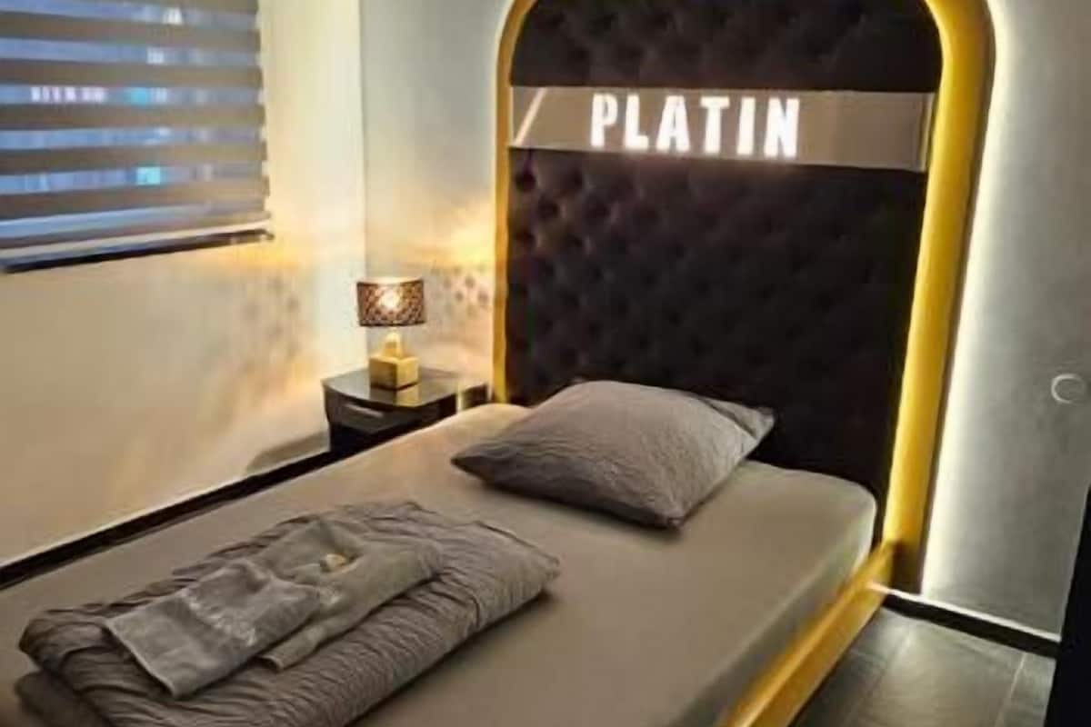Een moderne slaapkamer met een bed met een 'PLATIN' hoofdbord, een bedlampje en een netjes opgemaakt bed met een opgevouwen deken.
