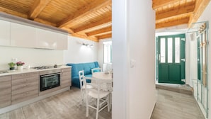 A modern kitchen with wooden beams, a dining area with a blue sofa, and a green door.