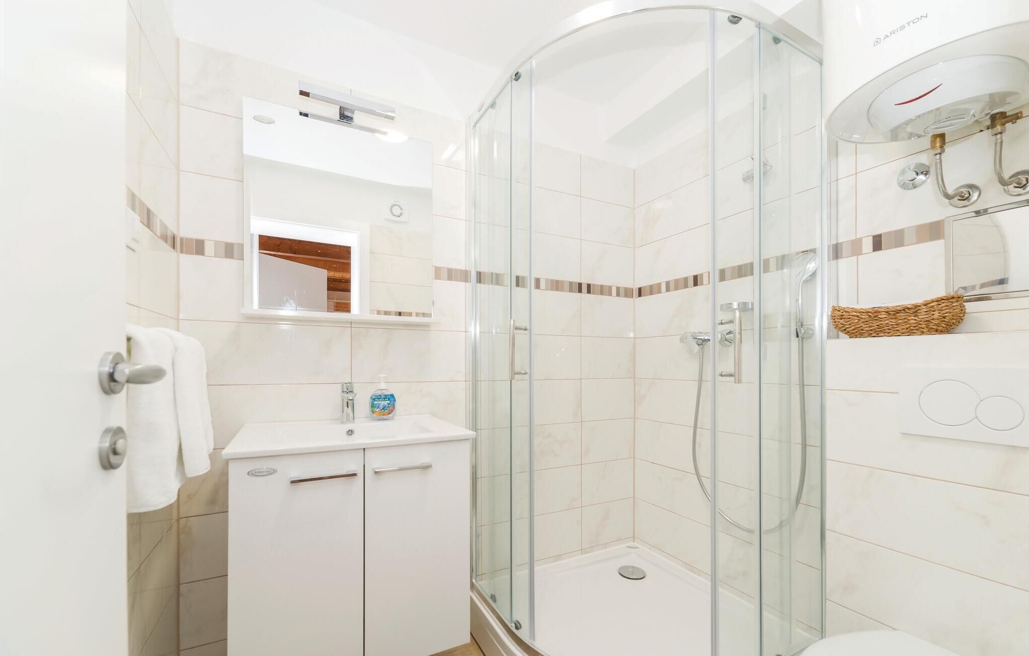A modern bathroom with a glass-enclosed shower, a white sink with a soap dispenser, and a mirror above the sink.