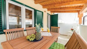 A wooden table with a pineapple and grapes, two glasses of orange juice, and green cushioned chairs.