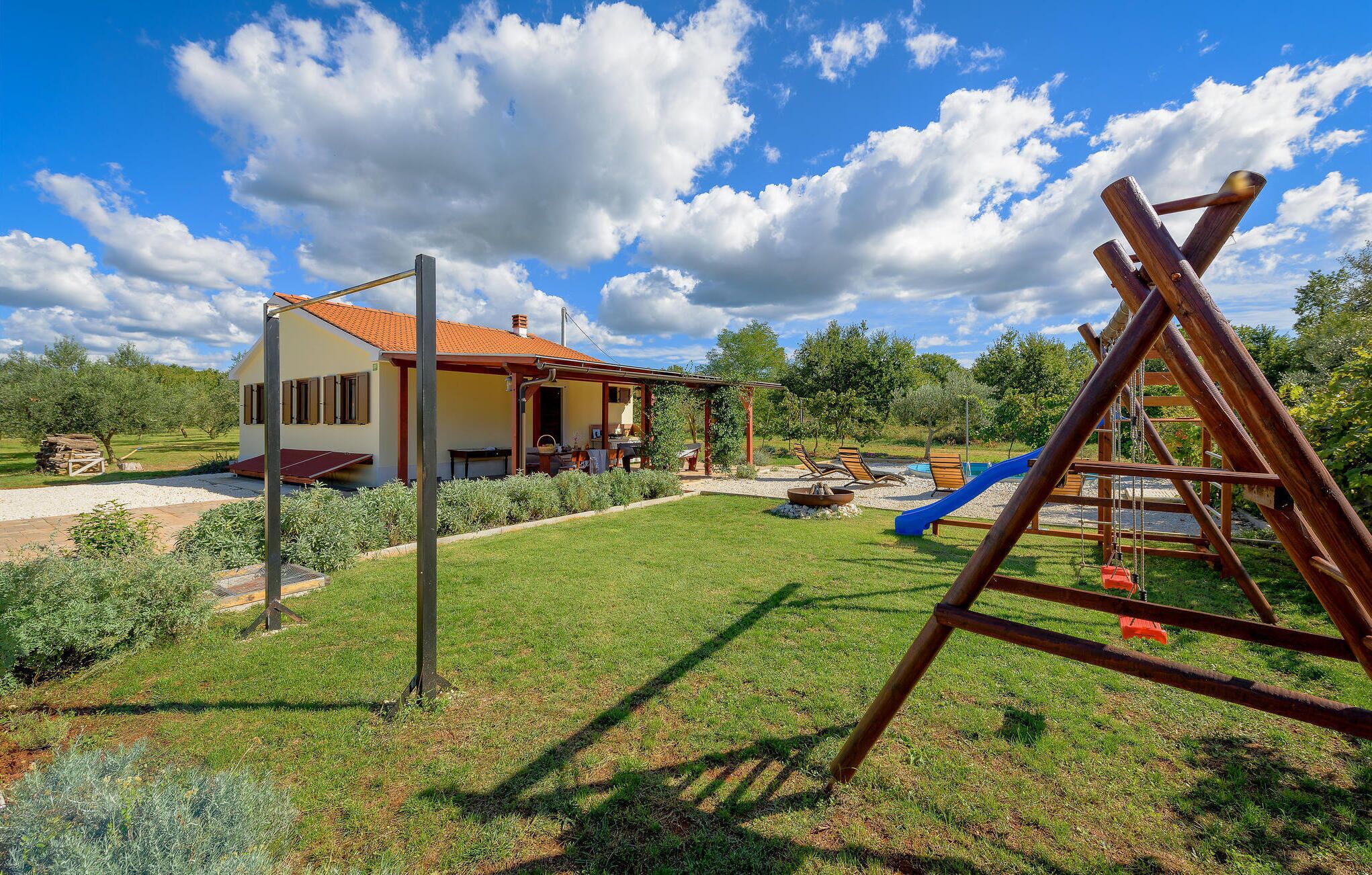 A house with a patio, a wooden swing set, and a blue slide in the yard.