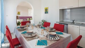 Un coin repas avec une table dressée pour quatre personnes, des chaises rouges et une cuisine équipée d’un évier en acier inoxydable et d’appareils électroménagers modernes.