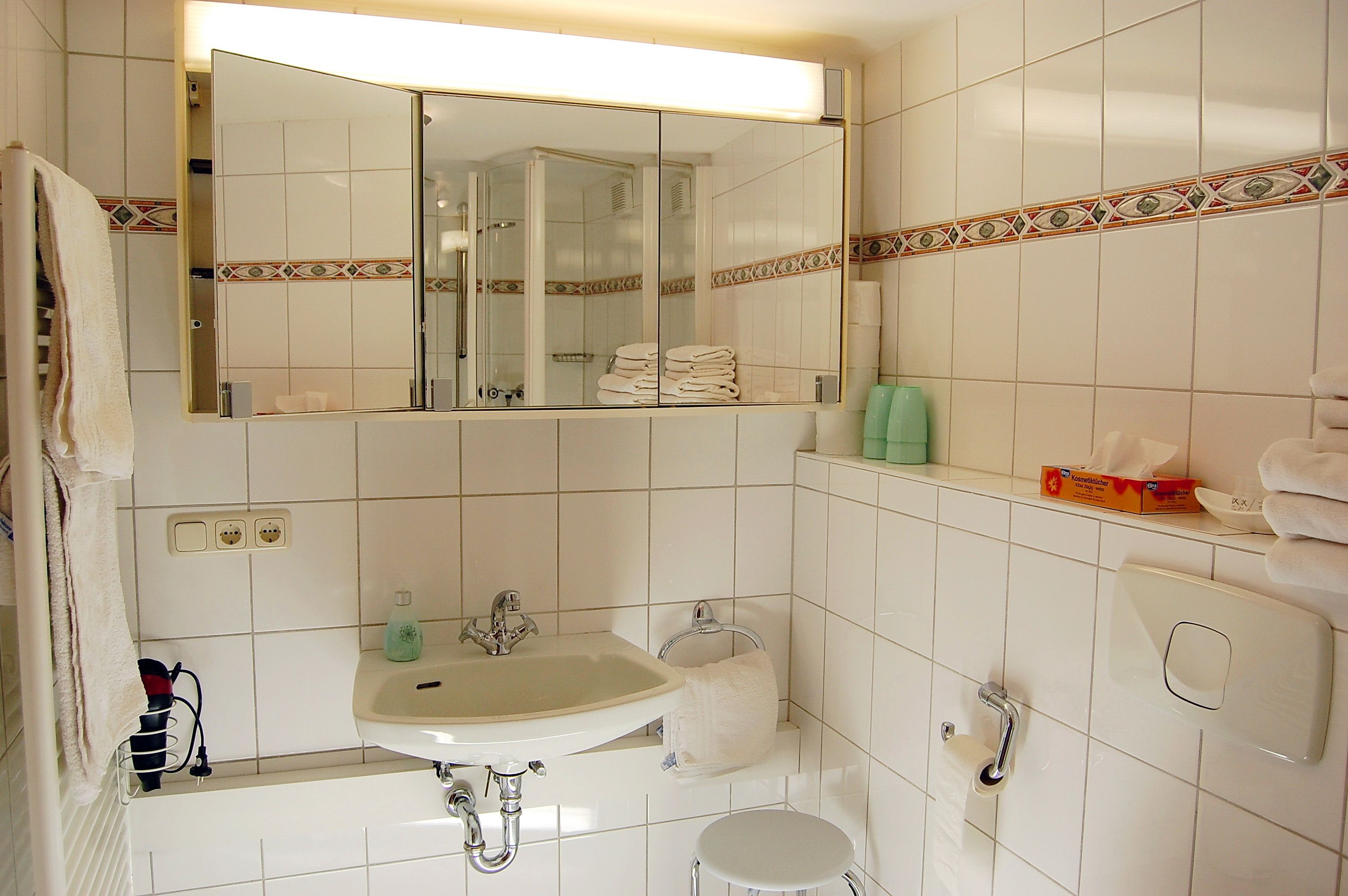 A bathroom with a sink, mirror, towel rack, and a shower visible in the reflection.