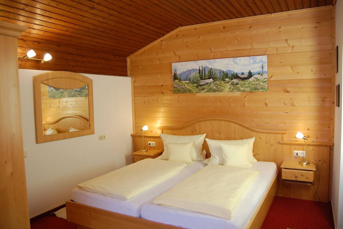 Une chambre aux murs lambrés, avec deux lits, deux tables de chevet et un miroir.