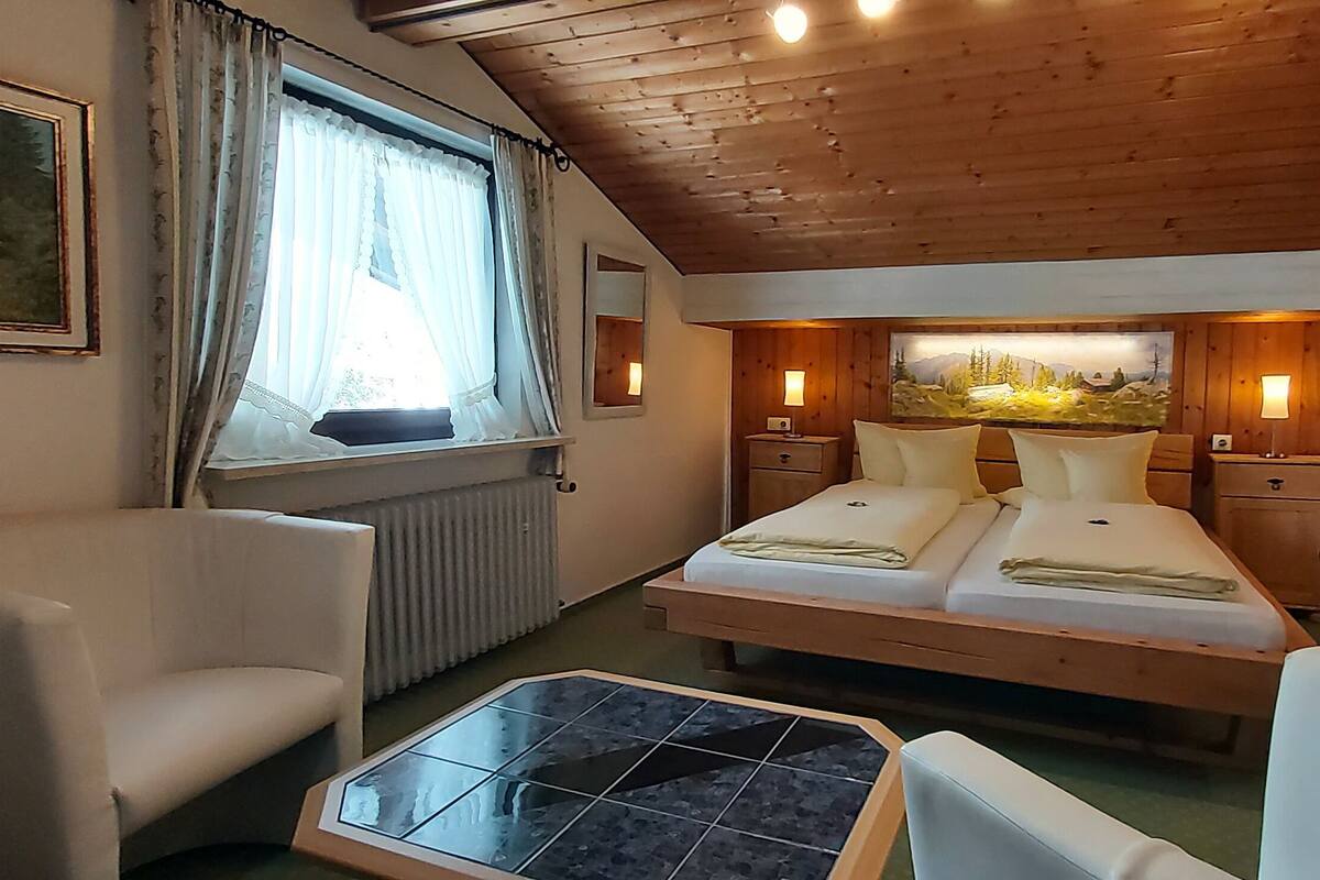 Une pièce confortable avec un lit, deux tables de chevet, une chaise, une petite table et une fenêtre avec des rideaux.