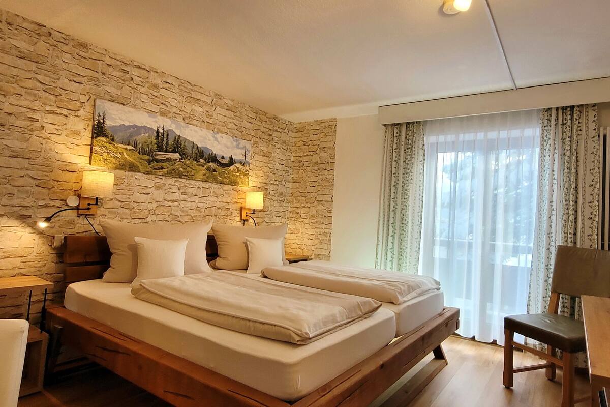Une chambre avec un mur en pierre, deux lits, une télévision et une table en bois.