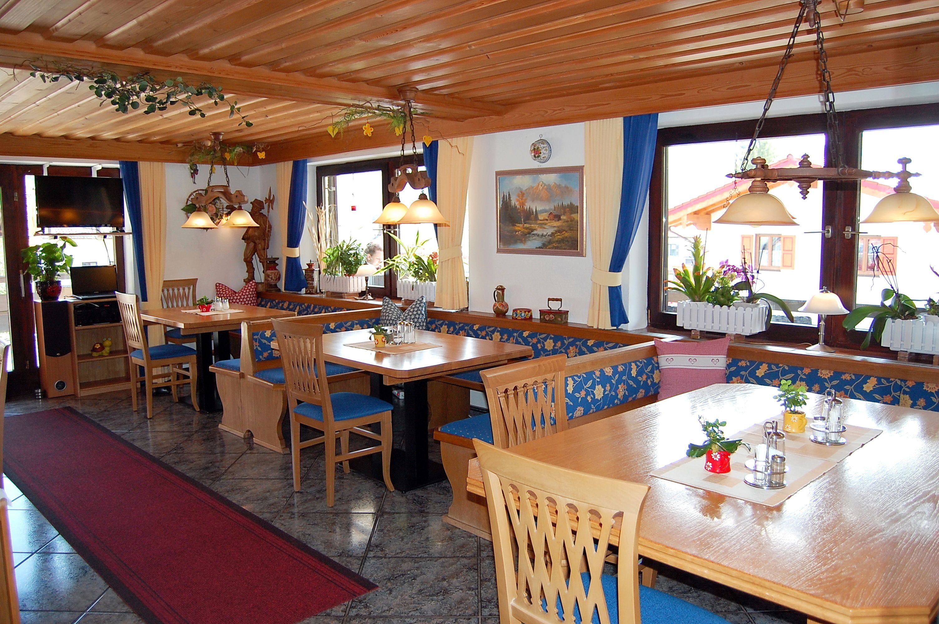 Ein Restaurant mit Holztischen und blau gepolsterten Sitzbänken, einem Fernseher und verschiedenen Pflanzen.