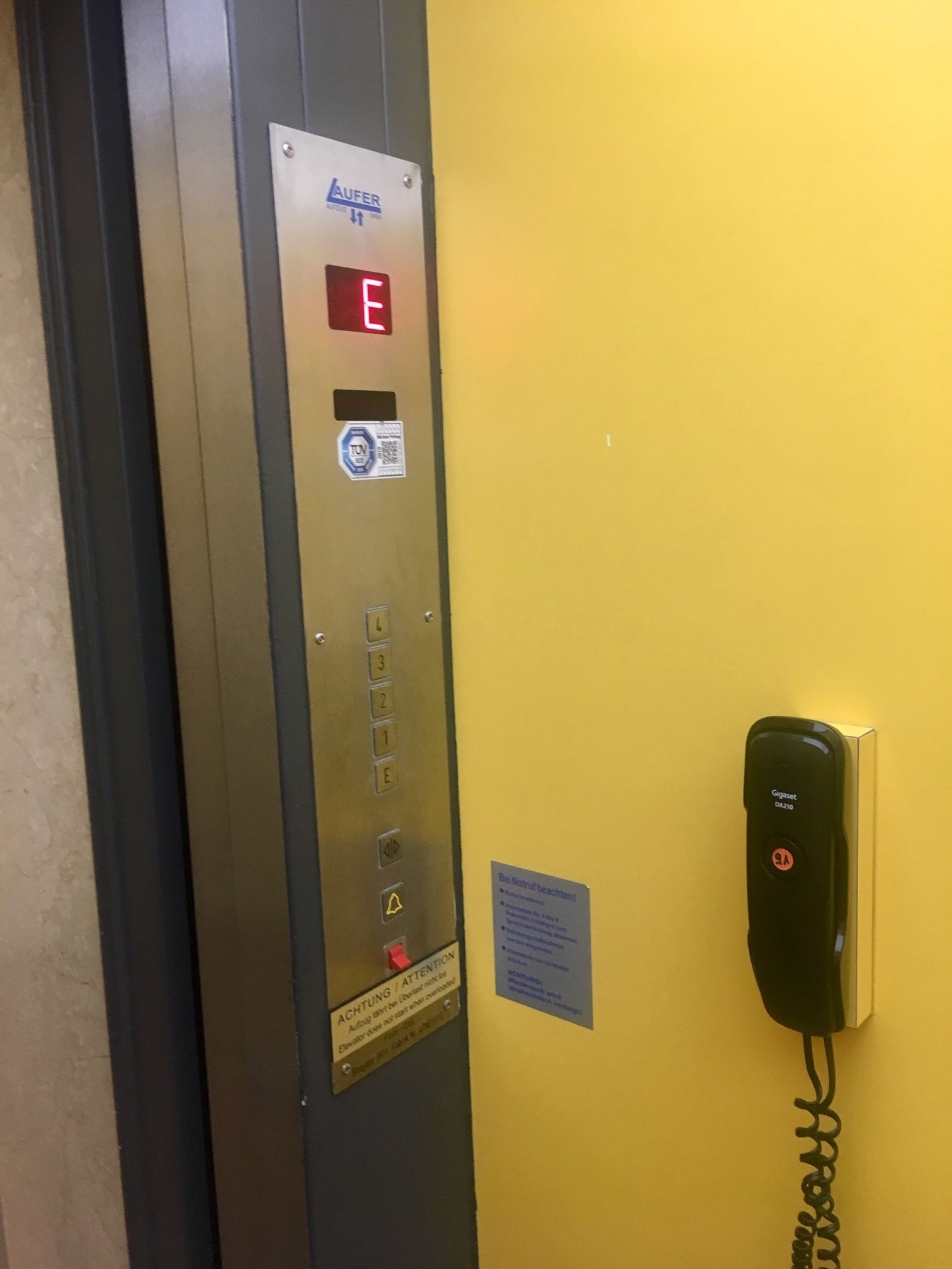 An elevator with a digital display indicating floor E, a control panel with buttons, and a security keypad.