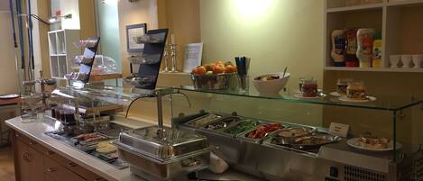 A buffet with various food items, including fruits, cheeses, and meats, displayed in glass containers.
