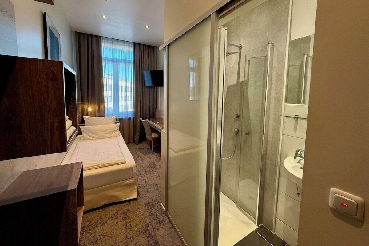 Una habitación de hotel con cama, escritorio, televisor, ducha con puerta de cristal y baño con lavamanos.