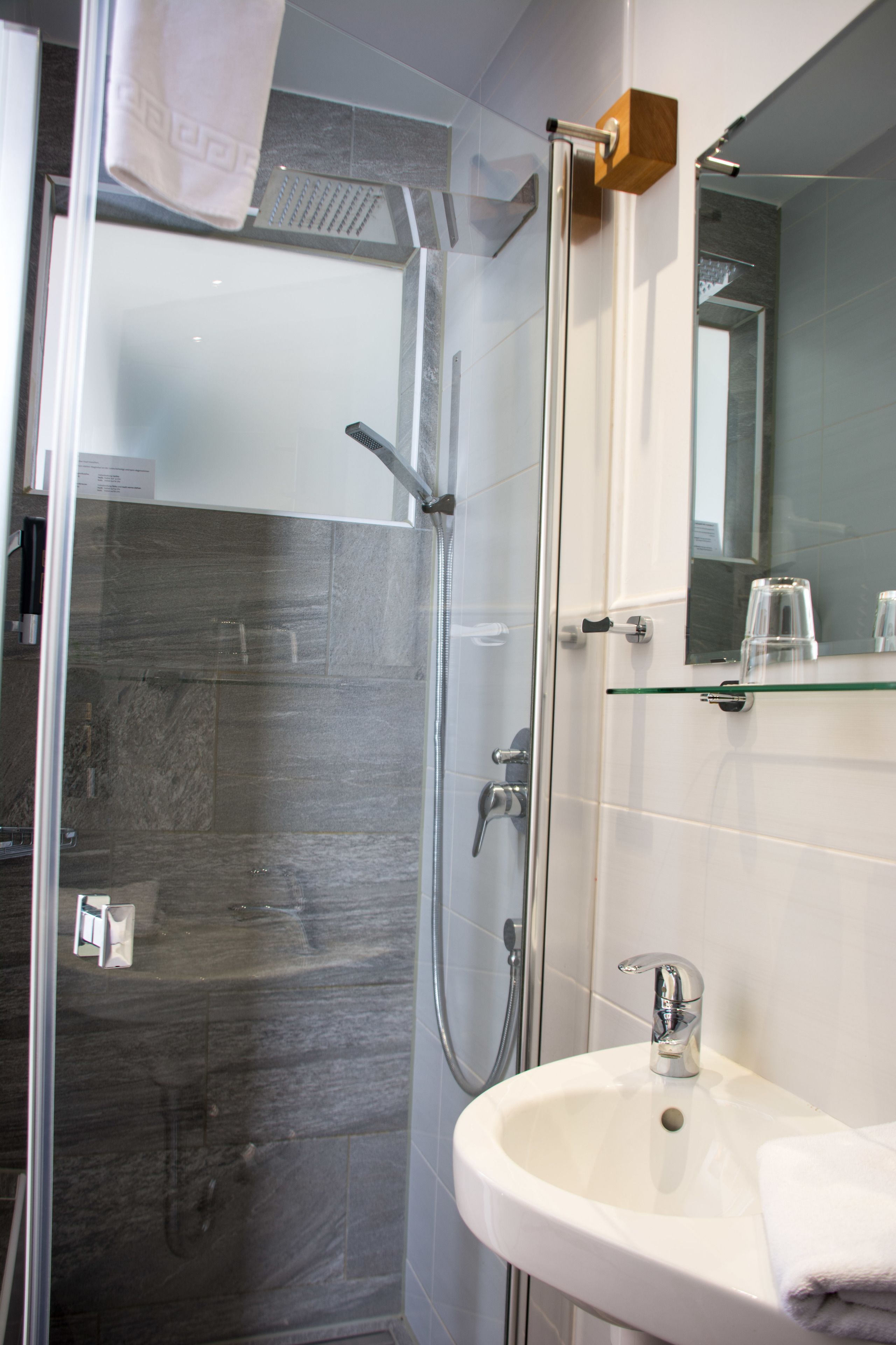 A modern bathroom with a glass-enclosed shower, a white sink, and a mirror above the sink.