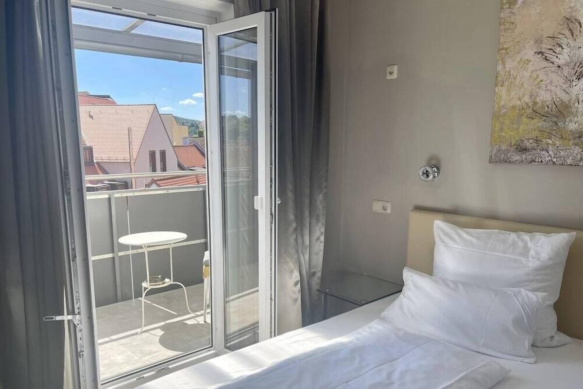 Una habitación de hotel con una cama, una mesita, una silla y una puerta corrediza de vidrio que da a un espacio al aire libre.
