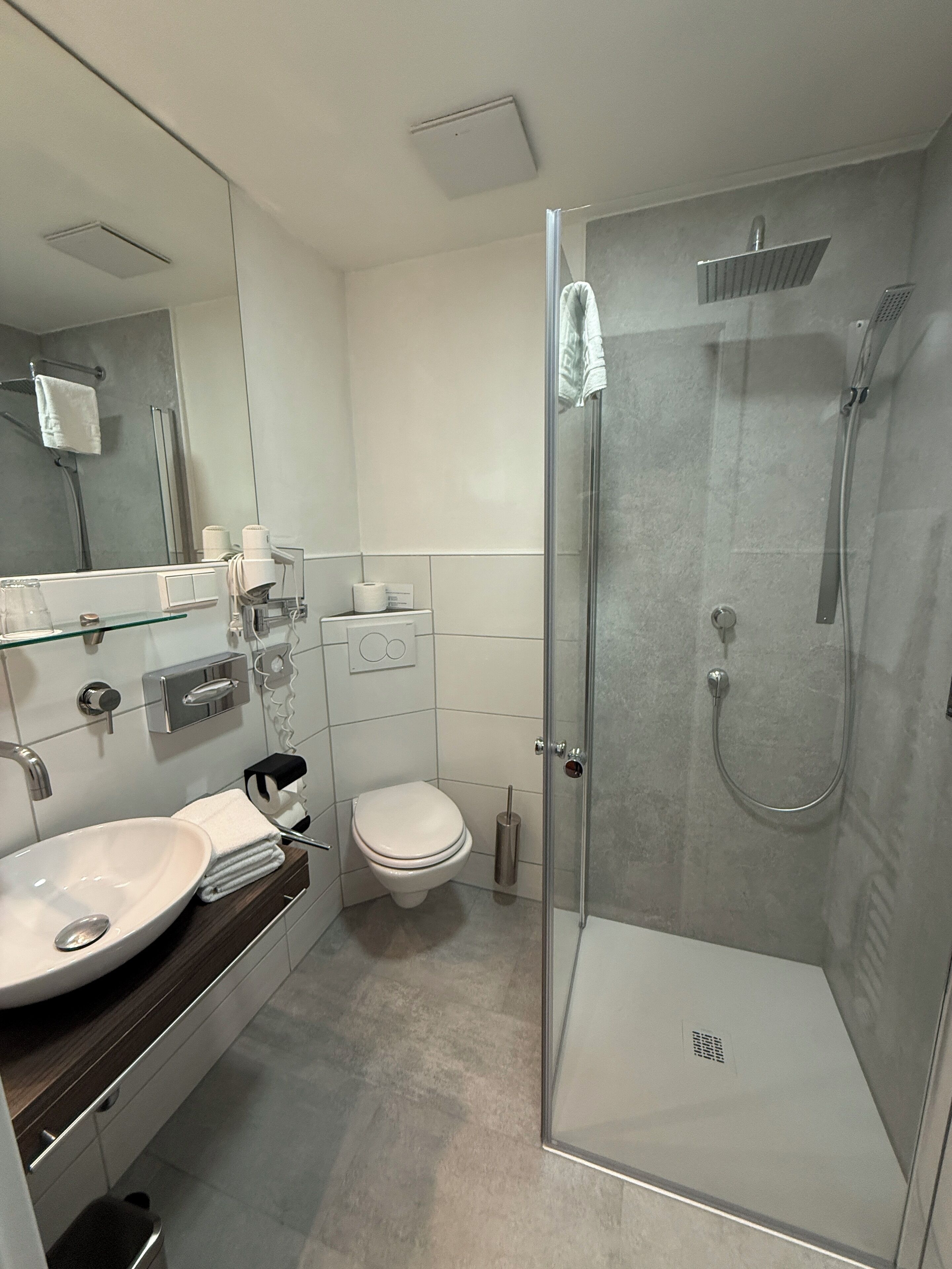 Un baño moderno con cabina de ducha de vidrio, un lavamanos blanco con espejo y un inodoro.