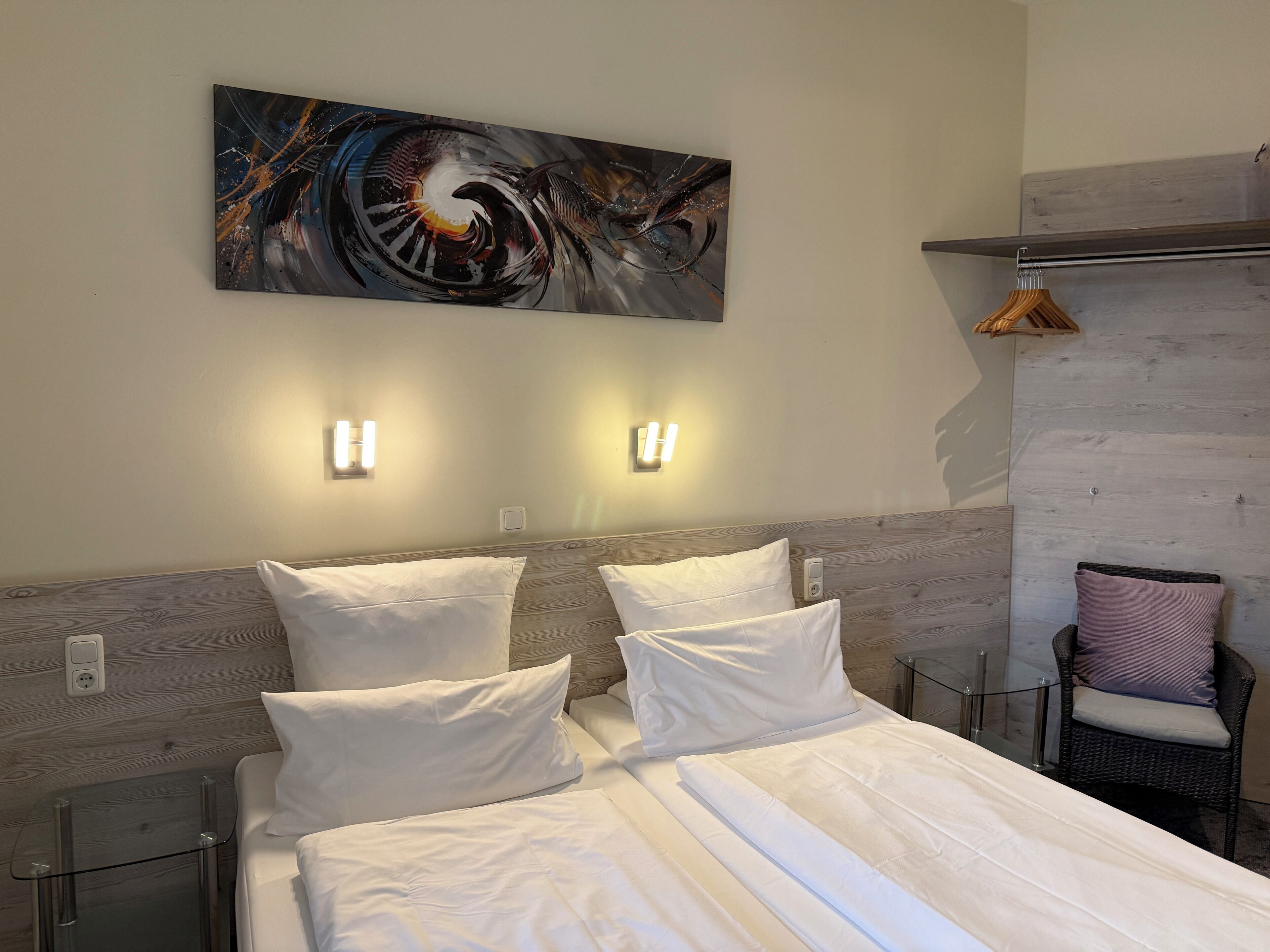 Habitación de hotel con una cama grande, dos mesitas de noche, un cuadro abstracto colgado en la pared y un cabecero de madera.
