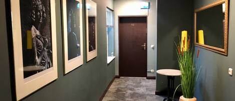 A hallway with framed artwork on the walls, a door labeled '40', a small round table with a vase of plants, and a mirror on the right wall.