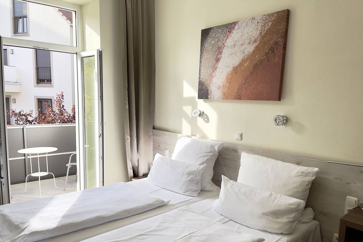 Habitación de hotel con cama, un cuadro en la pared y vista al balcón exterior.