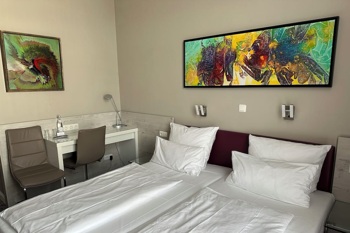 Una habitación de hotel con cama, escritorio, silla y dos cuadros.