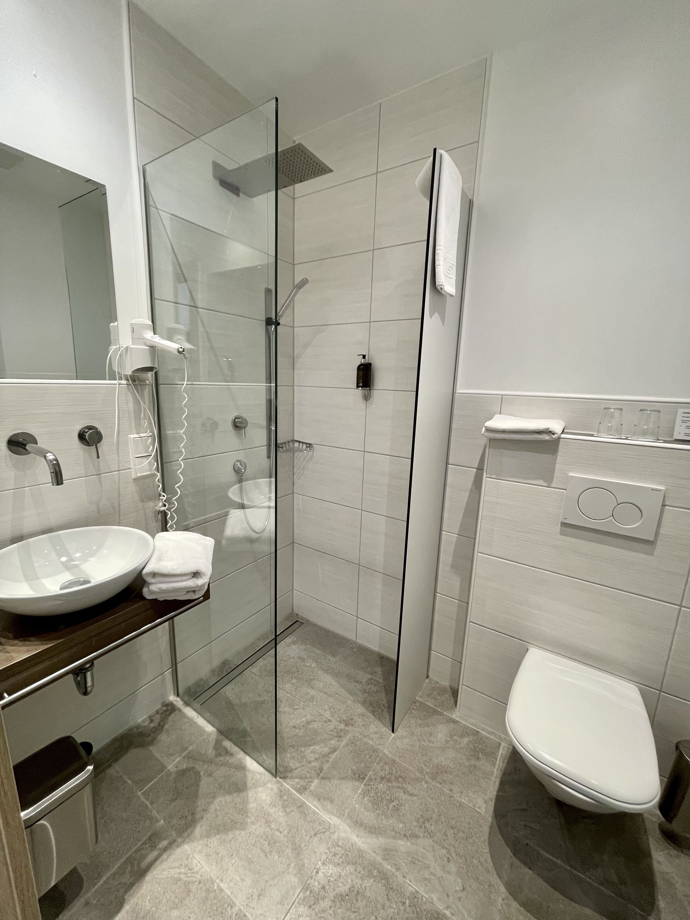 Un baño moderno con ducha de vidrio, un lavabo blanco con una toalla y un inodoro.