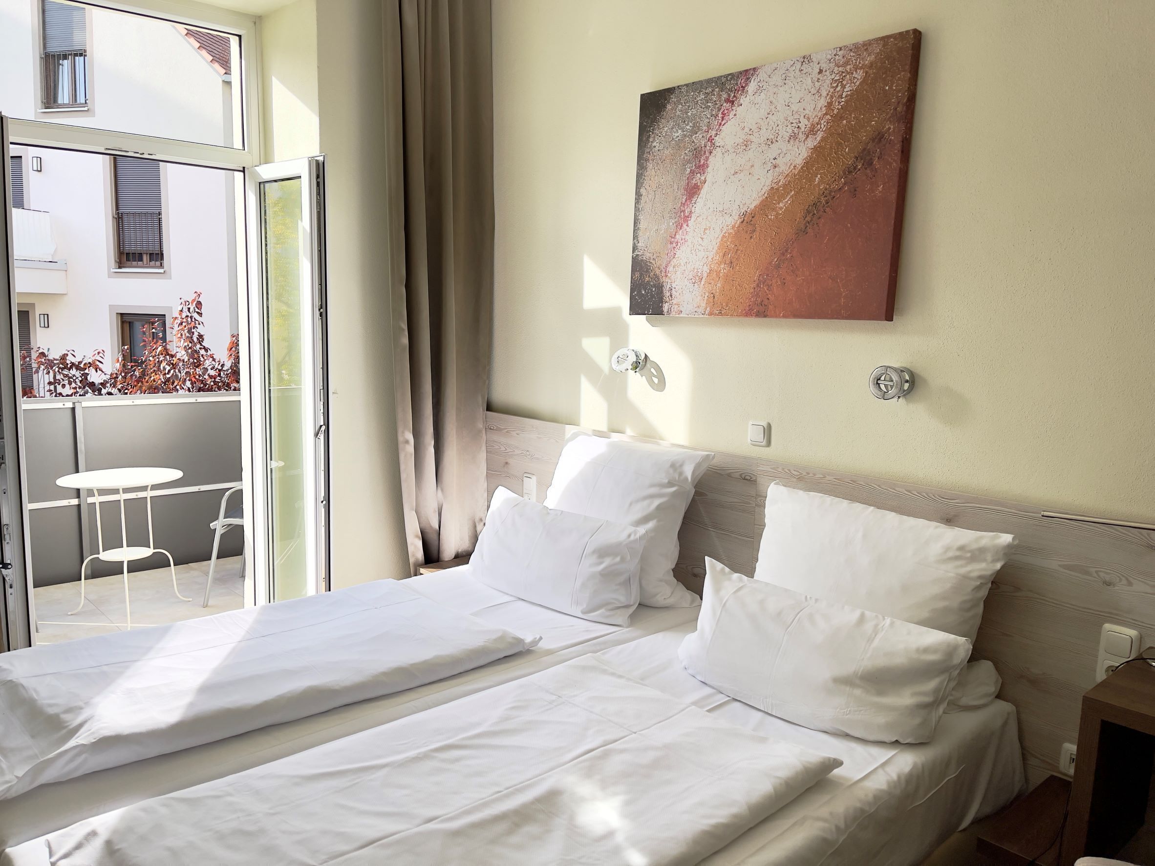Una habitación de hotel con una cama, un cuadro en la pared y un balcón con mesa y sillas.