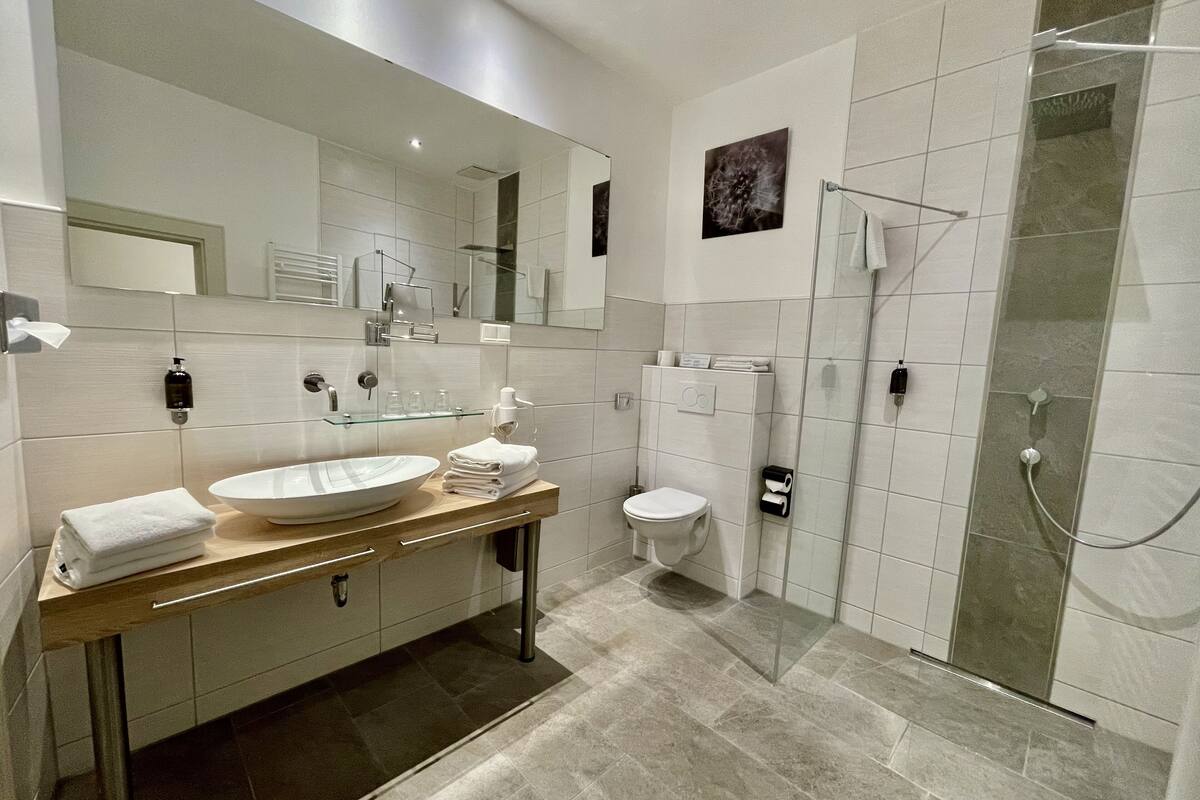 Un baño moderno con un espejo grande, un lavabo, un inodoro y una ducha con paredes de vidrio.