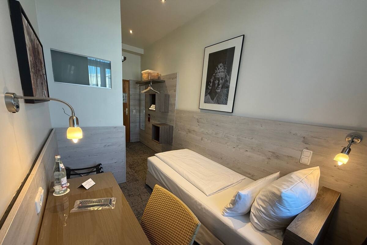 Una habitación de hotel con una cama, mesita de noche, lámpara y un cuadro en la pared.