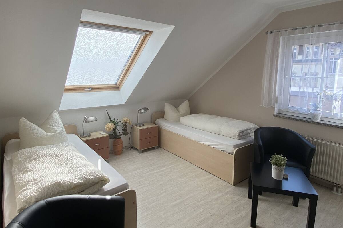 A bedroom with a skylight, a bed, a desk, a chair, and a radiator.
