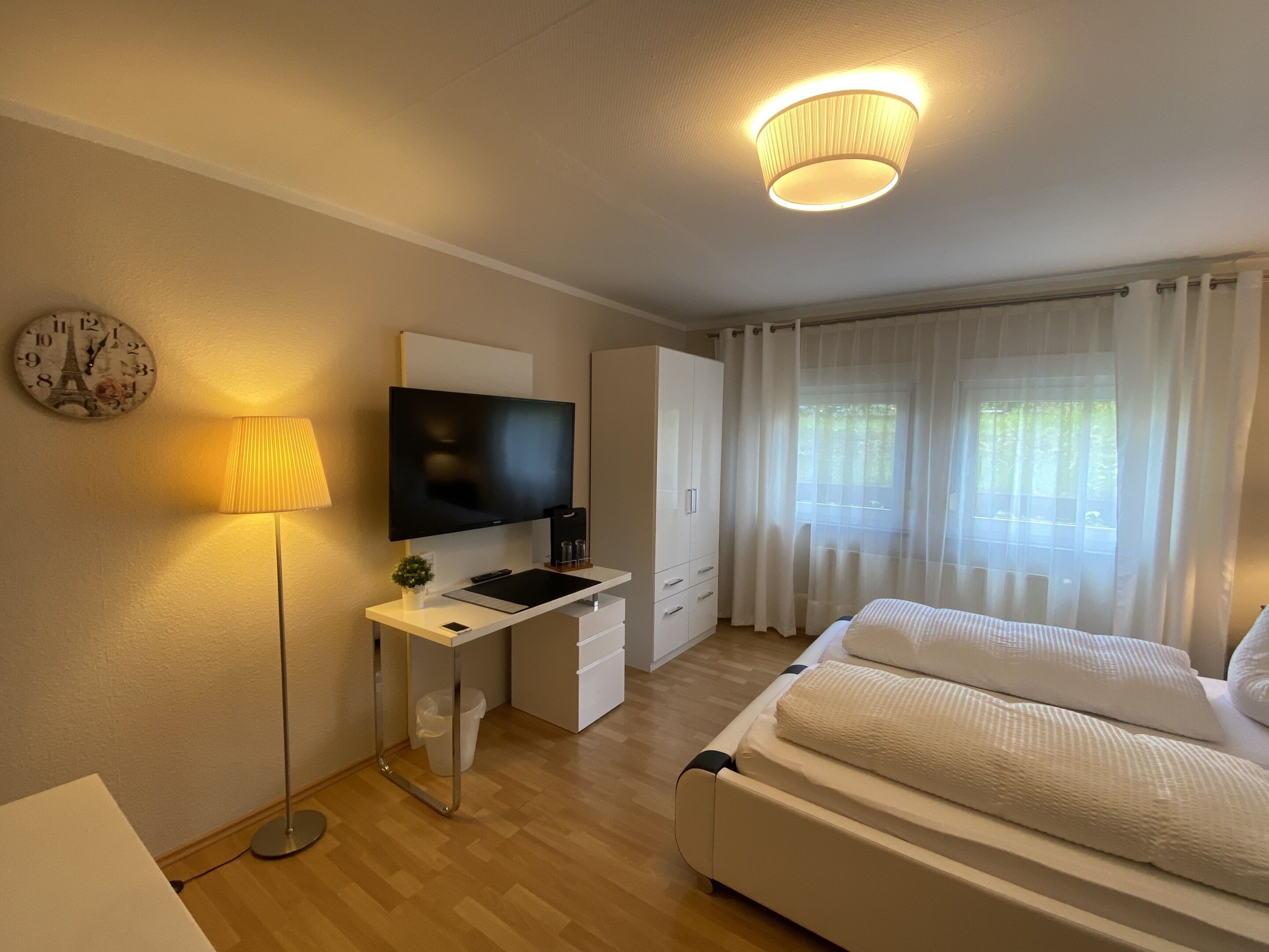 A modern hotel room with a bed, desk, TV, and curtains.