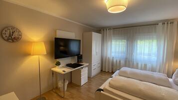 A modern hotel room with a bed, desk, TV, and curtains.