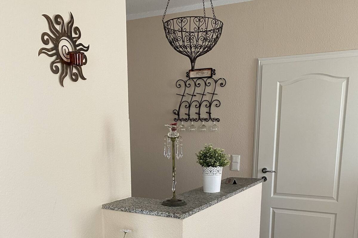 A reception area with a decorative metal wall piece, a hanging light fixture, a potted plant, and a floral arrangement.