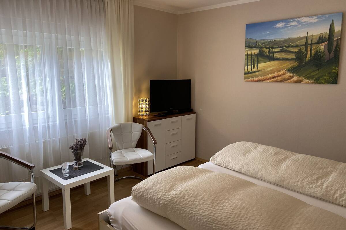 A hotel room with a bed, a desk with a chair, a television, and a painting on the wall.