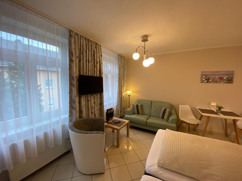 A hotel room with a bed, a green sofa, a small table, a chair, a TV, and a window with sheer curtains.